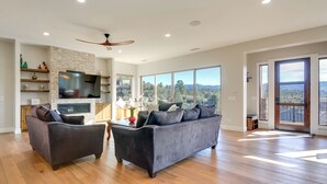 A spacious living room with a large gray sofa, a smaller armchair, a flat-screen TV, wooden flooring, and a view of the outdoors through large windows. - Prescott Vacation Rental w/ Game Room & Mtn Views! (Prescott)