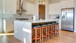 A modern kitchen with white cabinets, a stainless steel refrigerator, and a central island with bar stools. - Prescott Vacation Rental w/ Game Room & Mtn Views! (Prescott)
