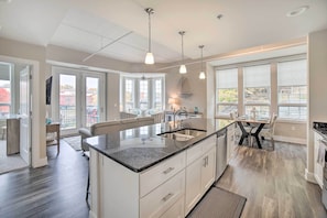 A spacious kitchen with a large island, pendant lighting, and a view of the city through large windows. - Luxe Manistee Condo w/ Balcony & River Views! (Manistee)