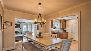 A dining area with a wooden table and chairs, a chandelier, and a view into the kitchen. - Mattituck Home w/ Fireplaces - Near Wineries (Mattituck)