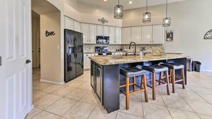 A modern kitchen with white cabinets, a black refrigerator, a granite countertop, and three bar stools. - Private Pool & Patio: Family Retreat in Mesa (Mesa)
