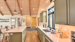 Una cocina moderna con vigas de madera, una isla central, taburetes de bar y un ventanal grande.