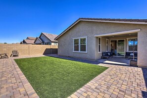 A residential backyard with a paved patio, artificial grass, and a brick wall. - Glendale Retreat: Walk to State Farm Stadium! (Glendale)