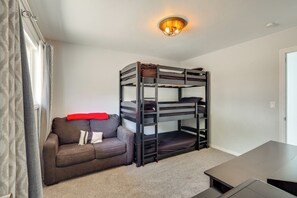 Una cama individual con un edredón rojo, un sofá con cojines y una mesa en una habitación con paredes blancas y una lámpara en el techo.