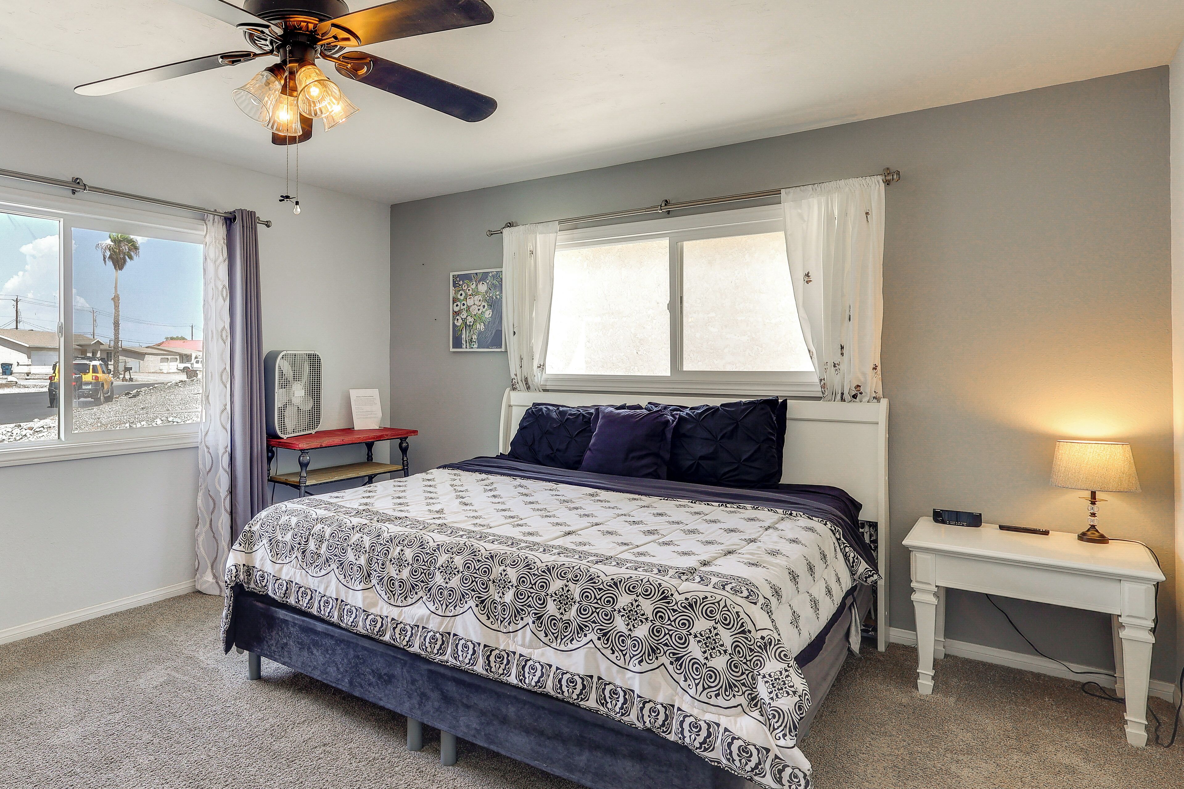 A bedroom with a bed, a bedside table, a lamp, a ceiling fan, and a window with curtains.