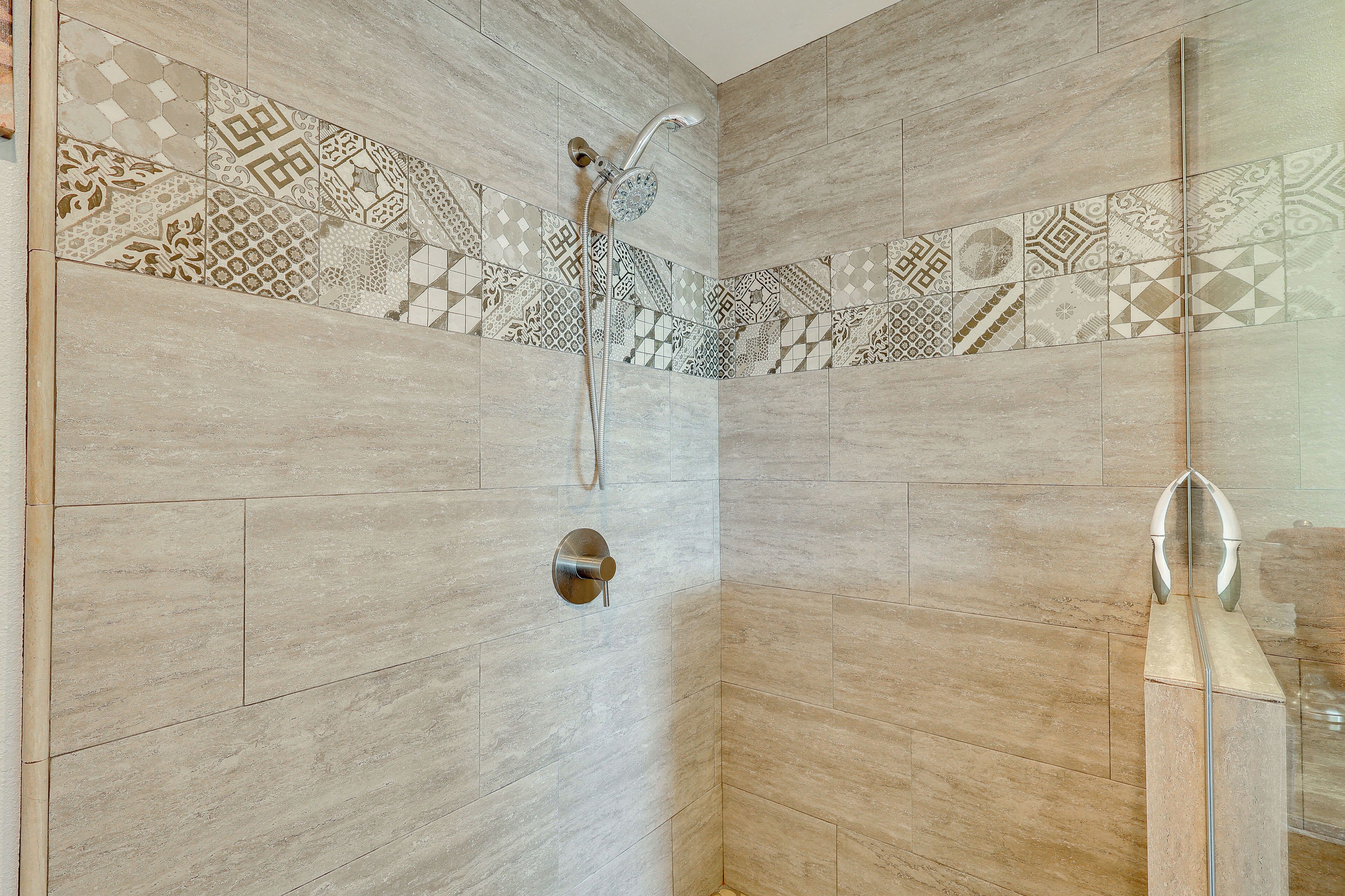 A shower with a handheld showerhead and a wall-mounted control.