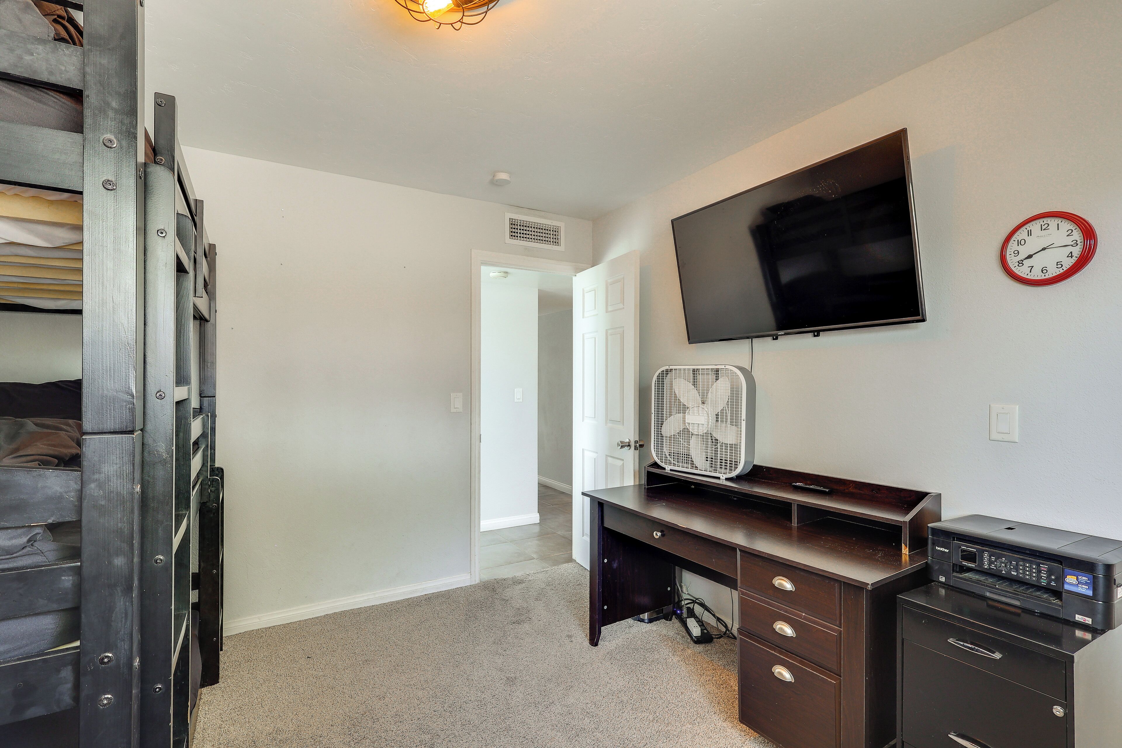 A room with a flat-screen TV mounted on the wall, a desk with a computer, and a clock.