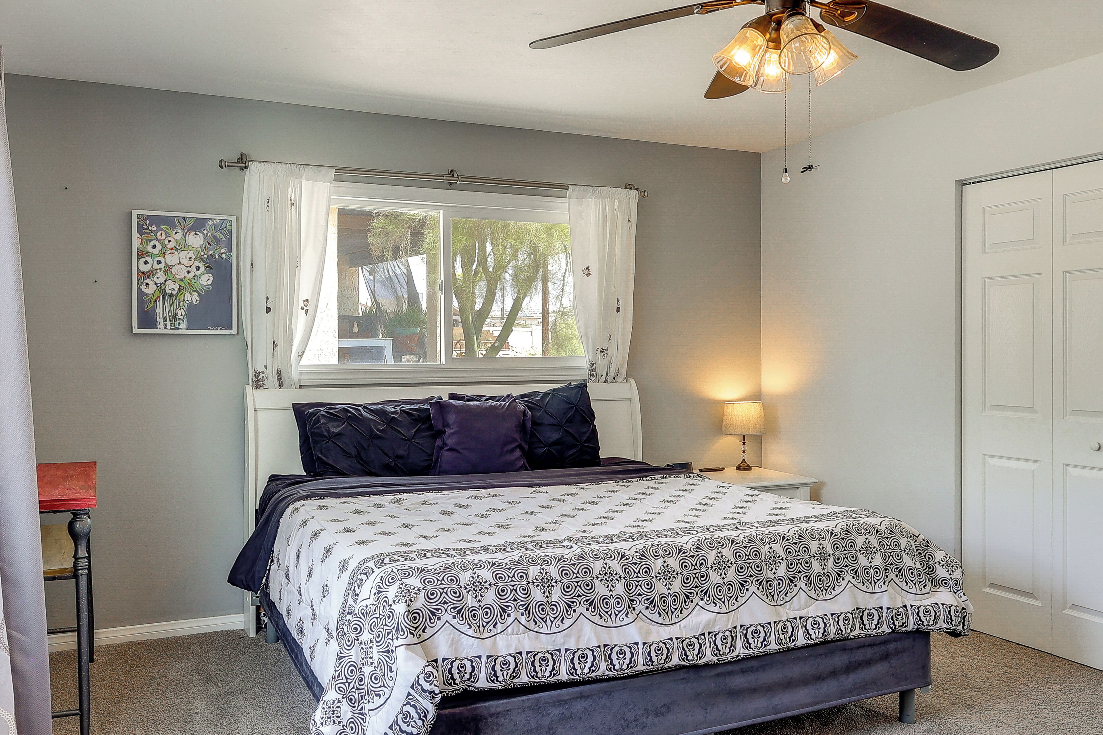 A bedroom with a bed, a window with curtains, a ceiling fan, a bedside lamp, and a door.