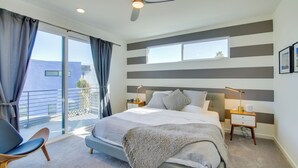 A modern bedroom with a large bed, a ceiling fan, a nightstand with a lamp, and a view of the outside balcony. - Modern Oasis w/ Mtn-view Pool Deck - Walk Downtown (Palm Springs)
