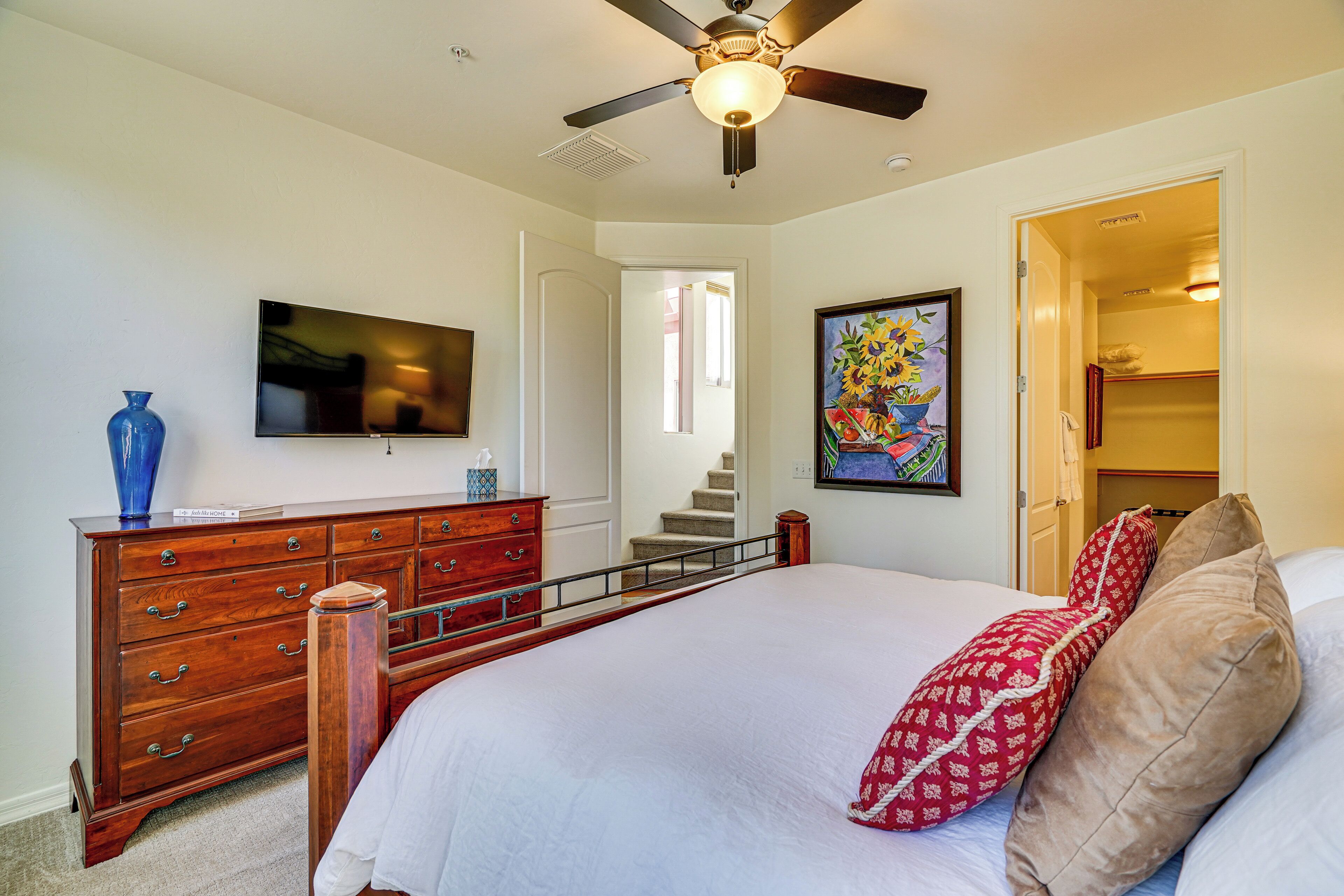 A bedroom with a bed, a dresser, a television, and a painting.