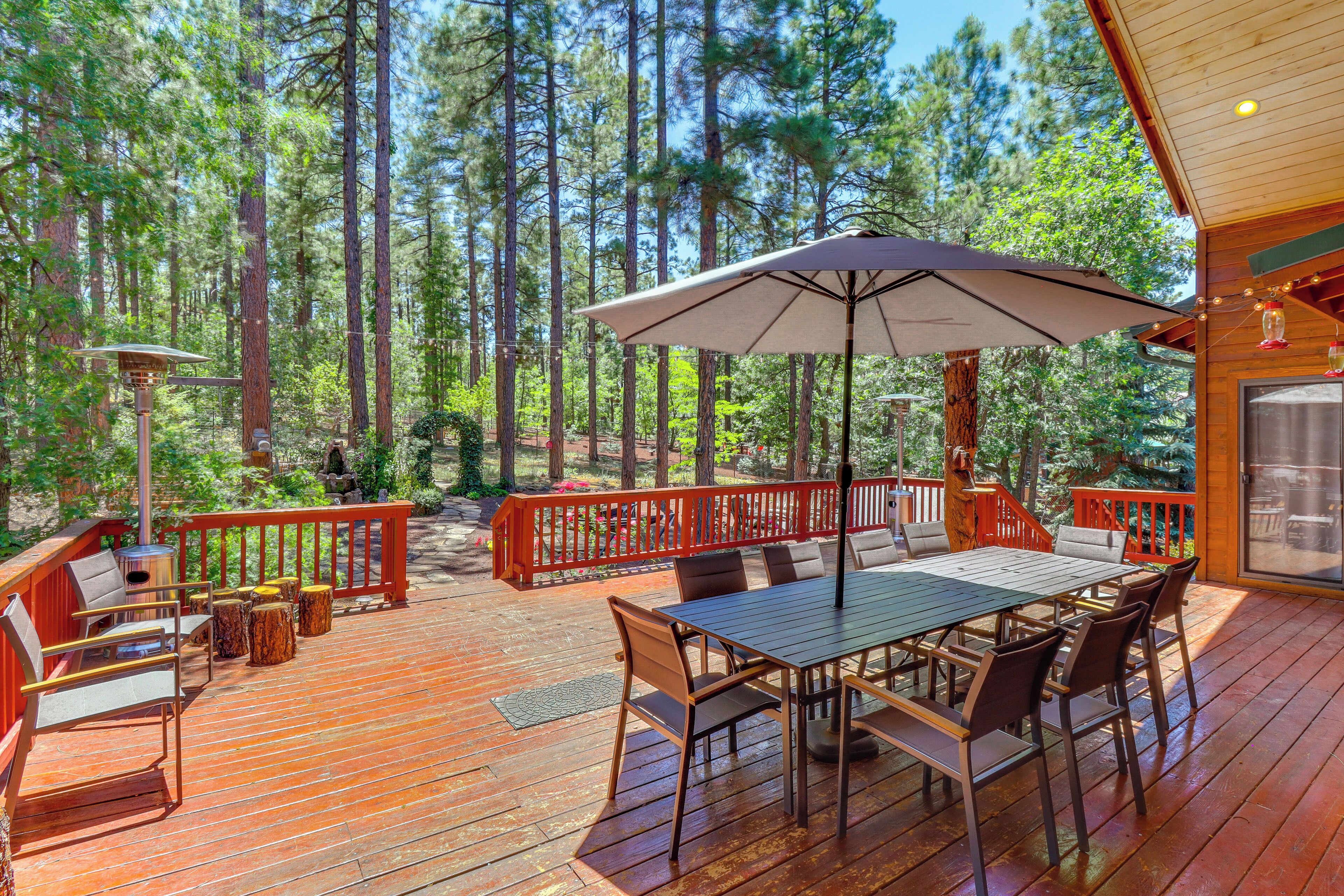 A wooden deck with a table and chairs, surrounded by a red railing, overlooking a forest.