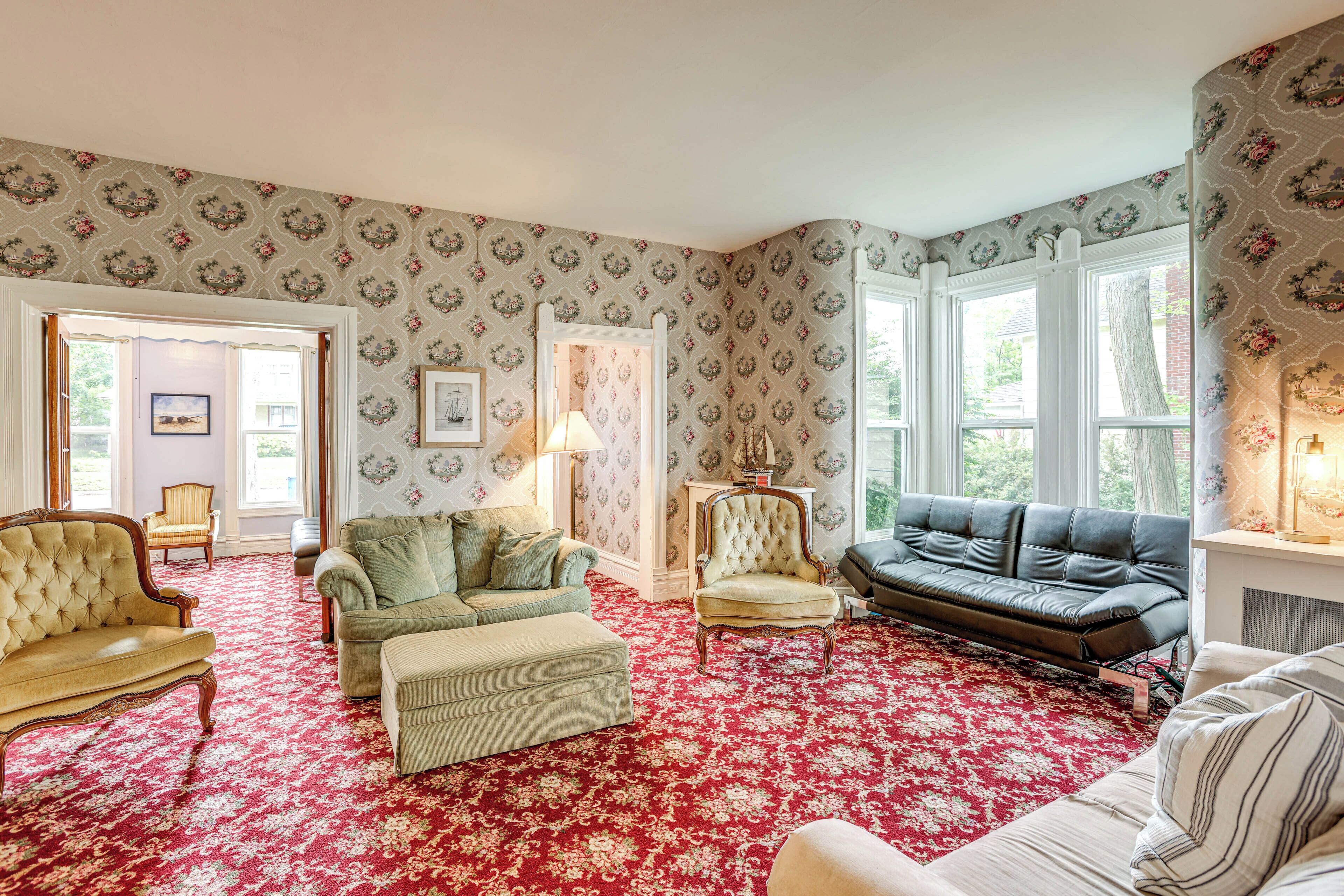A living room with a red floral carpet, a green armchair, a beige sofa, and a black leather sofa.