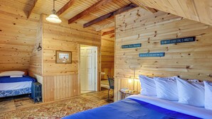 A wooden cabin room with two beds, a radiator, a rug, and a door leading to another room. - Walk to Lake Michigan & Dtwn: Coastal Grand' (Ludington)