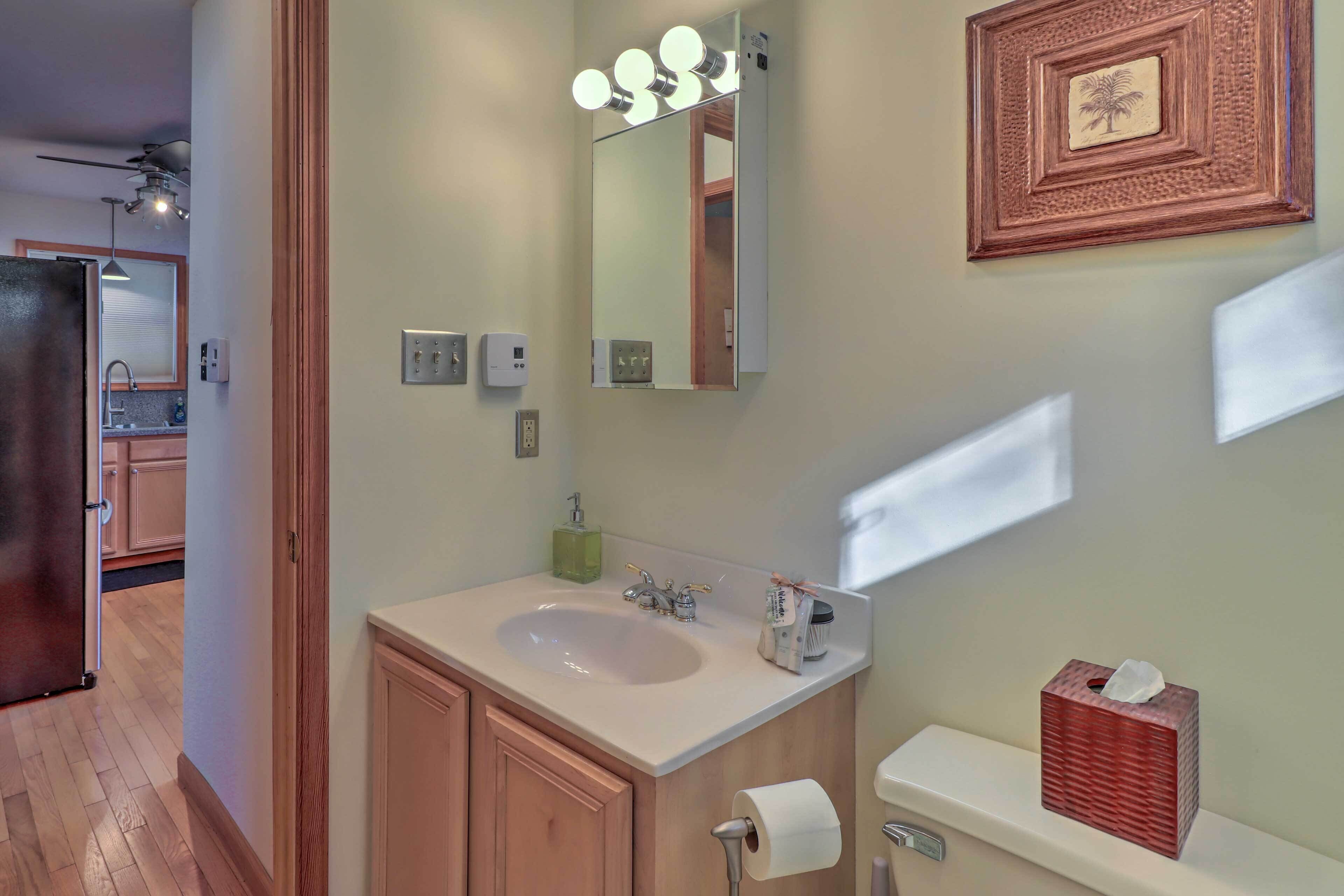 A bathroom with a sink, mirror, and toilet. There is a towel dispenser and a tissue box on the counter.