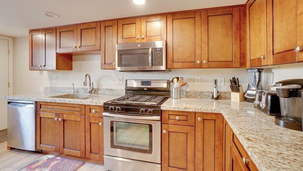 A modern kitchen with wooden cabinets, stainless steel appliances, granite countertops, and a dishwasher. - Flagstaff Townhome w/ Grill ~ 3 Mi to Downtown! (Flagstaff)