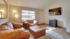 A spacious living room with a large window, a flat-screen TV mounted on the wall, and a dark wooden cabinet. - Flagstaff Townhome w/ Grill ~ 3 Mi to Downtown! (Flagstaff)
