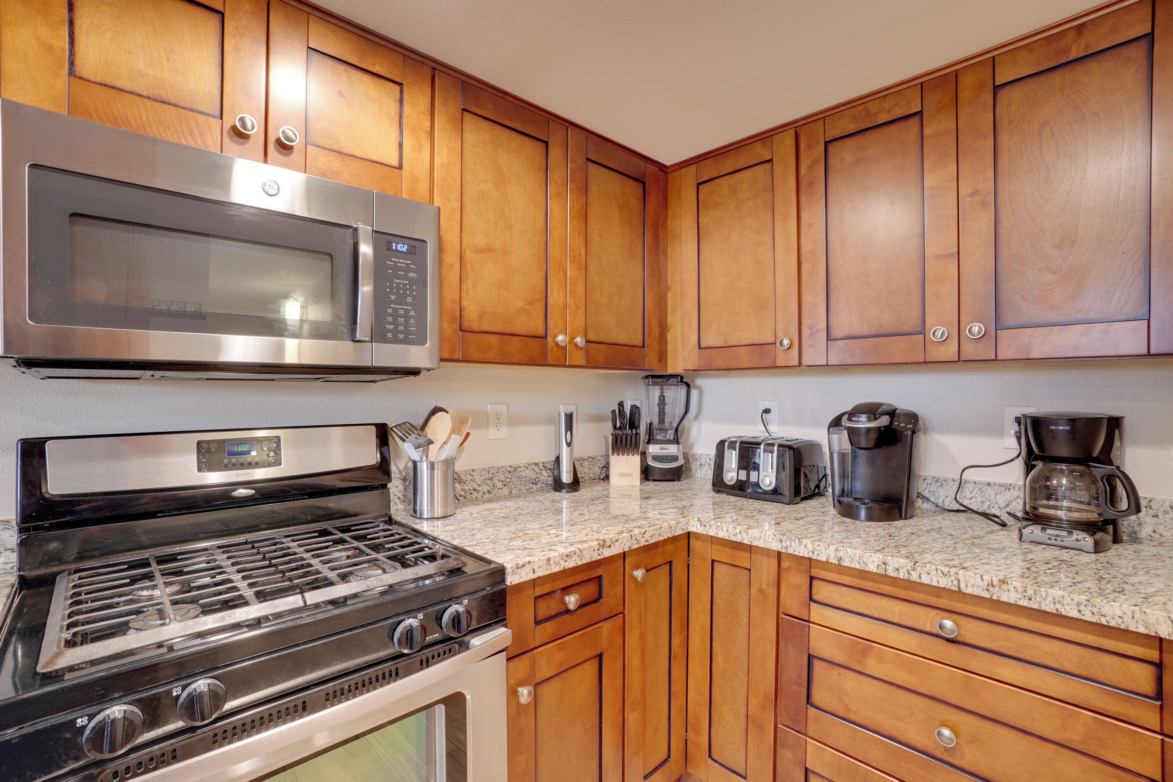 A kitchen with wooden cabinets, a stainless steel microwave, a gas stove, a coffee maker, and a toaster.