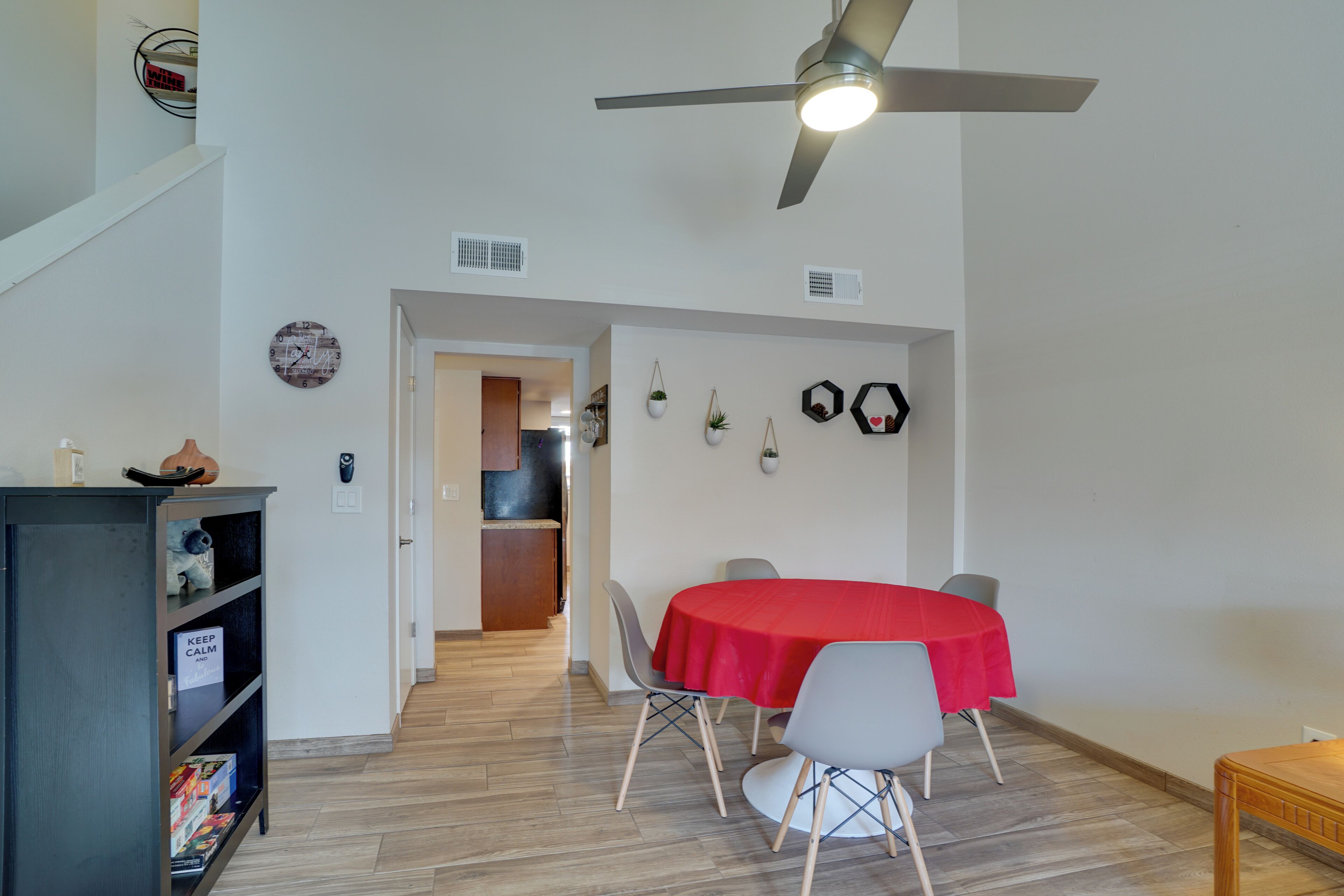 A dining area with a red tablecloth, a ceiling fan, and a bookshelf.