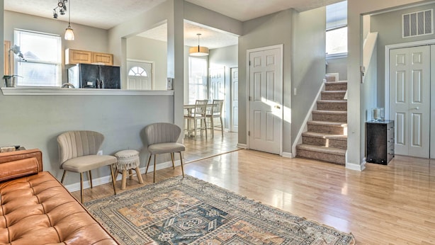 A spacious living room with a brown leather couch, two chairs, a patterned rug, and a kitchen area in the background. - Cozy Indianapolis Home w/ Private Hot Tub! (Indianapolis)