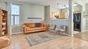 A living room with a brown leather sofa, a patterned rug, wooden flooring, and a kitchen area with wooden cabinets and a black refrigerator. - Cozy Indianapolis Home w/ Private Hot Tub! (Indianapolis)
