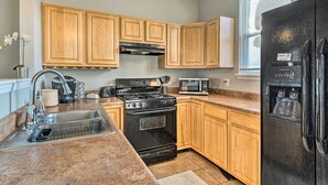 A kitchen with wooden cabinets, a stainless steel sink, a black stove, a microwave, and a refrigerator. - Cozy Indianapolis Home w/ Private Hot Tub! (Indianapolis)