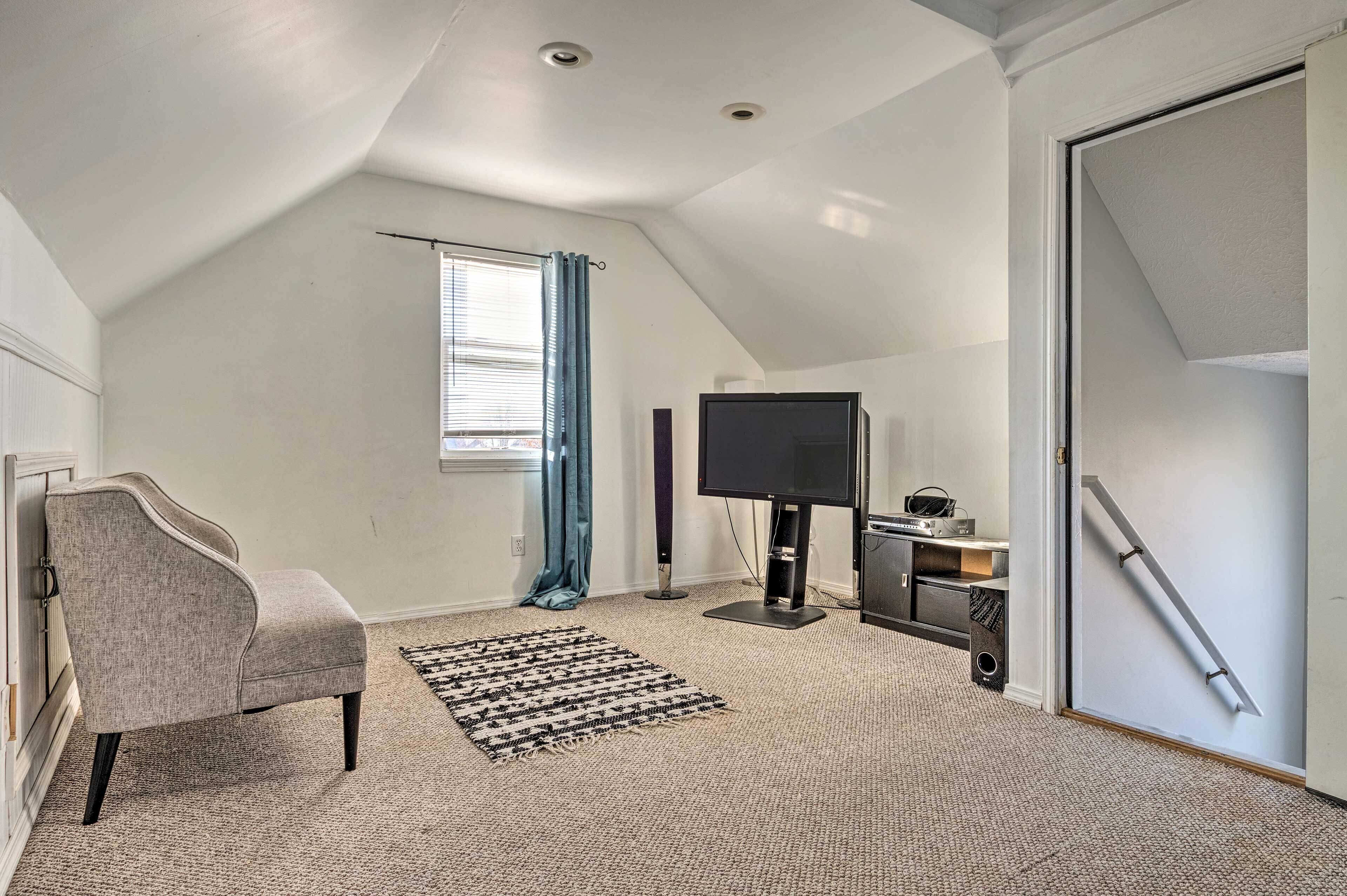 A room with a sloped ceiling, a television, a chair, a rug, and a door with a handrail.