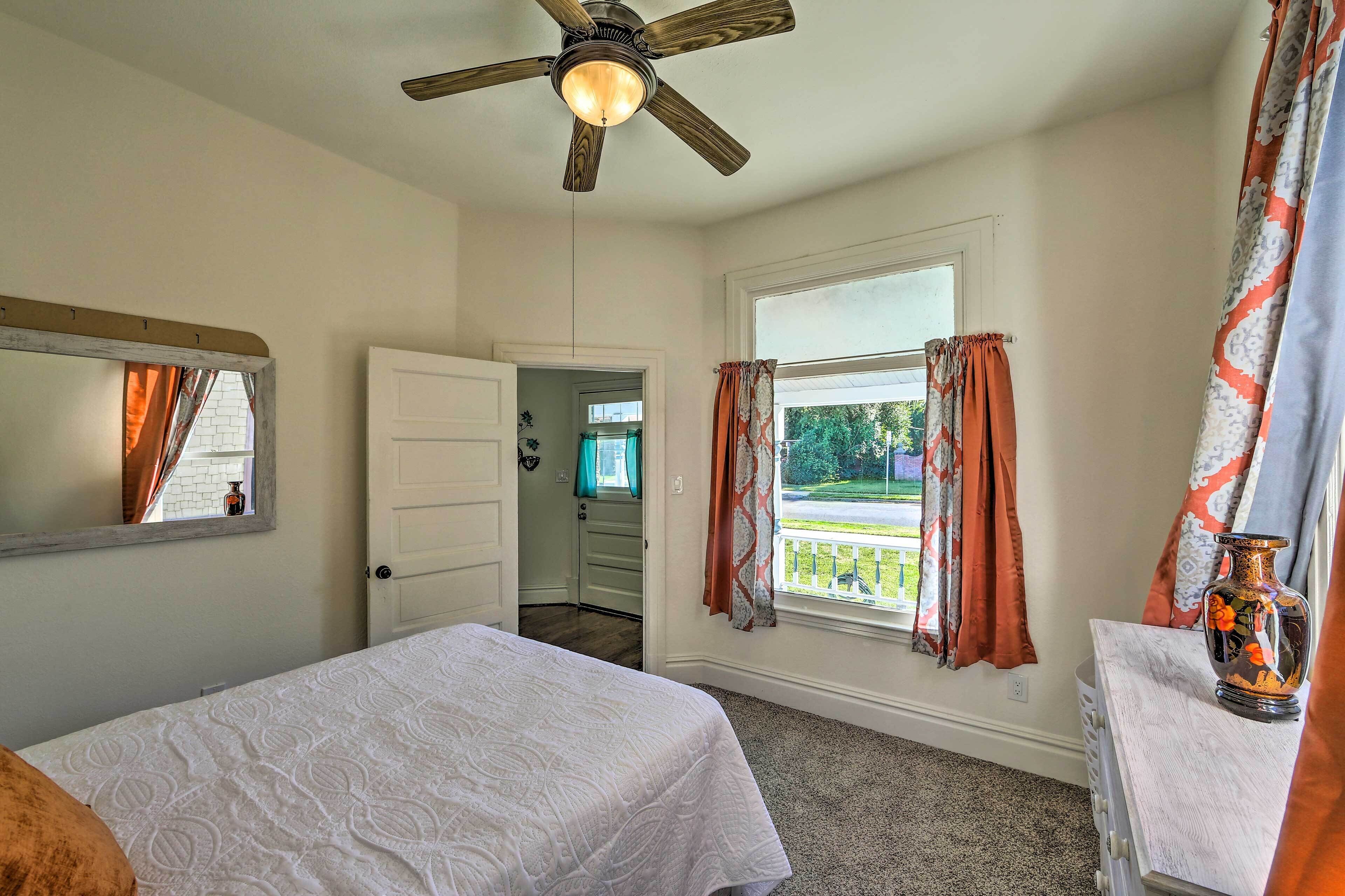 A bedroom with two beds, a ceiling fan, a window with curtains, and a view of the outside.