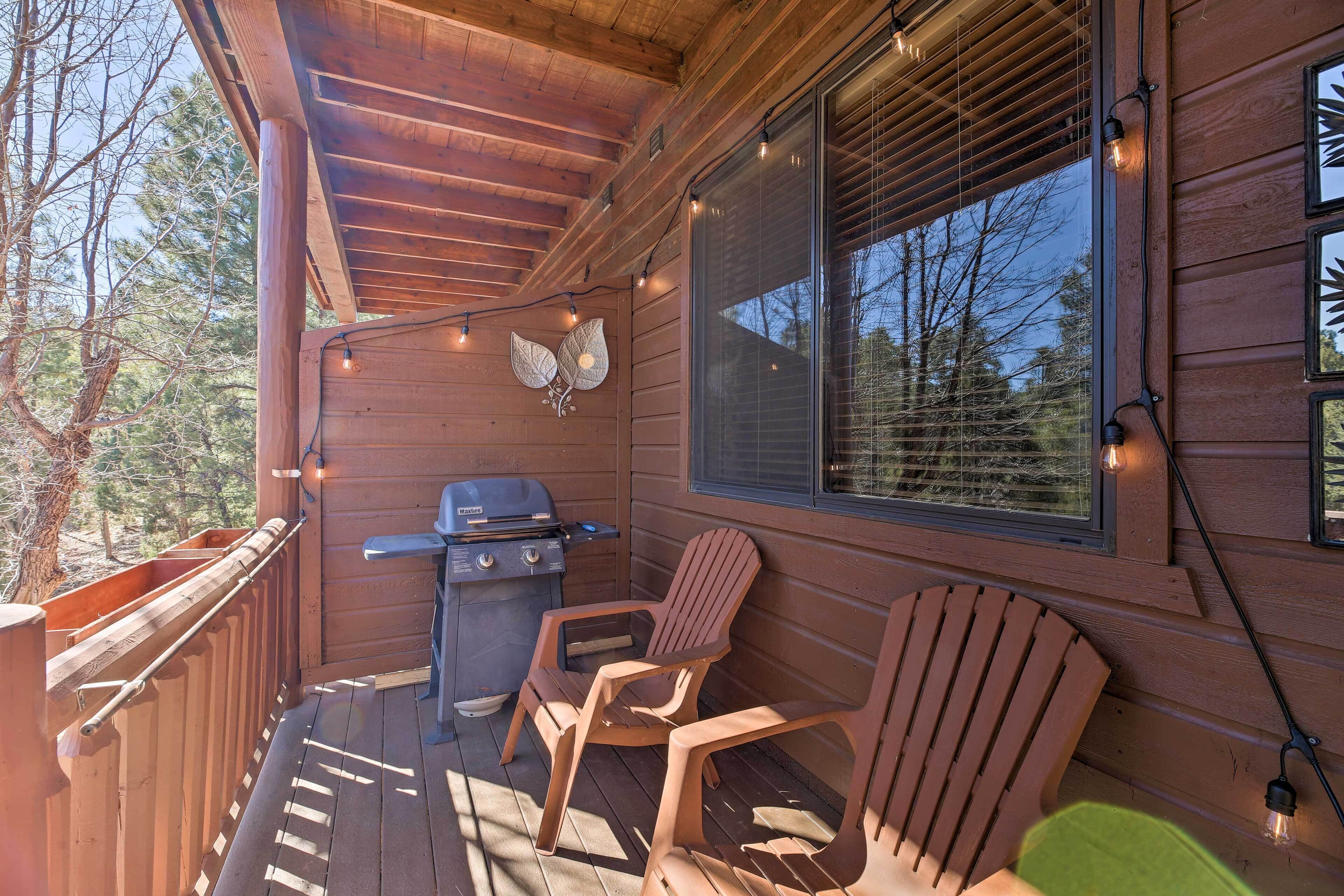 A wooden deck with a grill, two Adirondack chairs, and string lights.