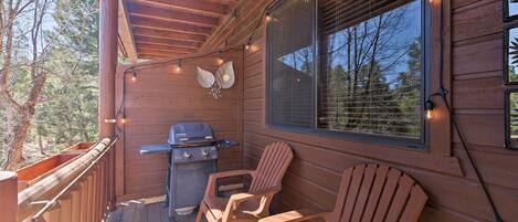 A wooden deck with a grill, two Adirondack chairs, and string lights.