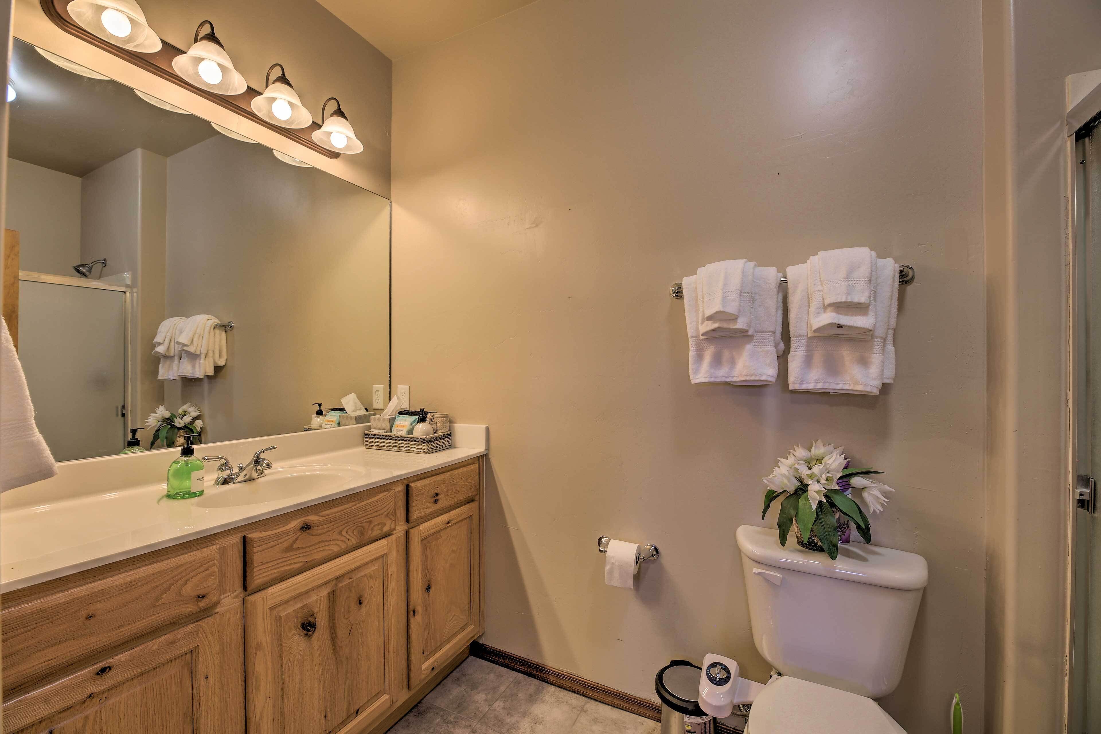 A bathroom with a wooden vanity, a white sink, a mirror, and a toilet with a plant on top.