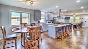 A spacious kitchen with a central island, grey cabinets, and a dining area with wooden chairs and a table. - Newly Built Cotter Home, Great Fishing Nearby (Cotter)