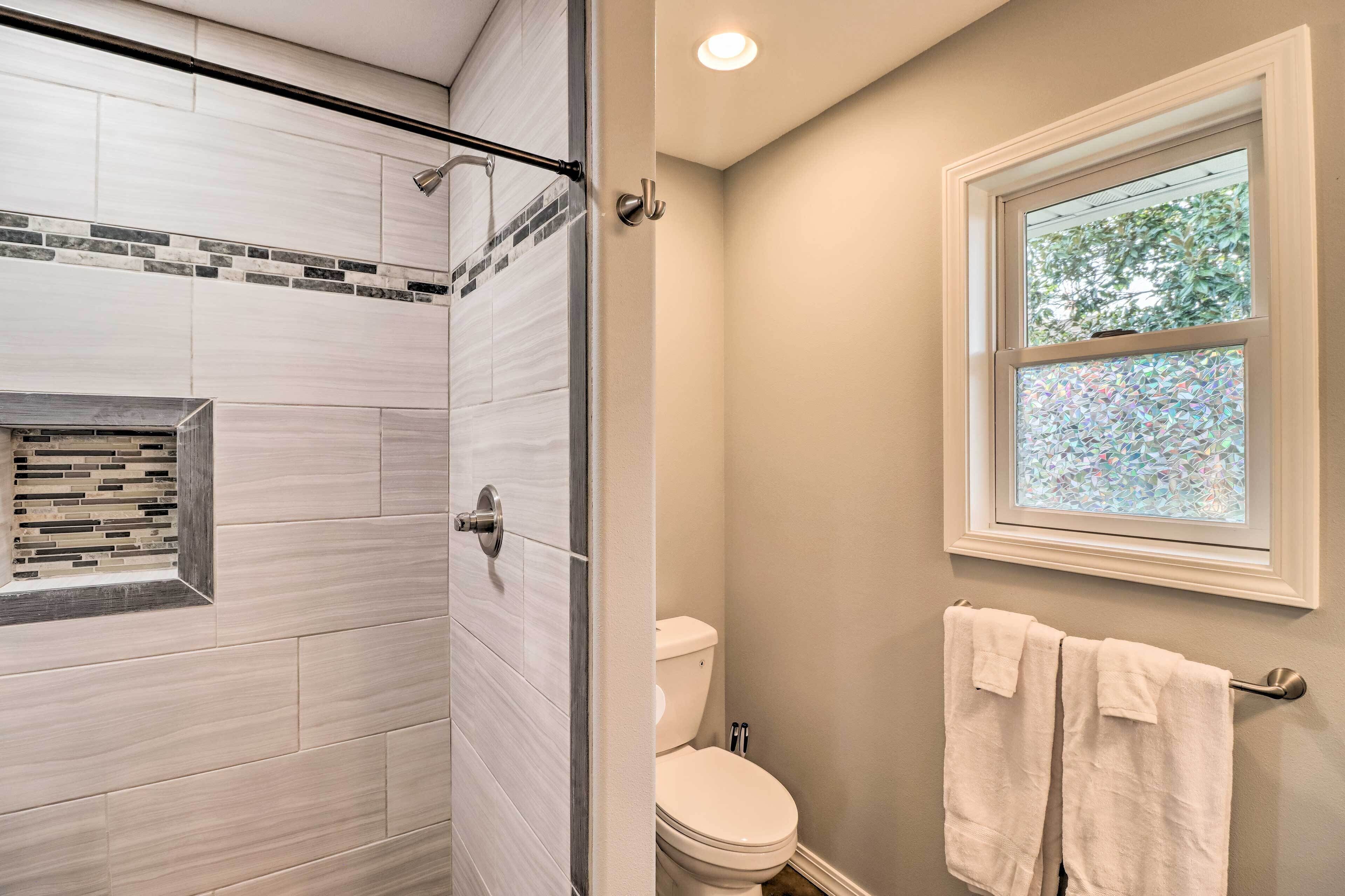 A bathroom with a shower, toilet, and a window with a view of trees.