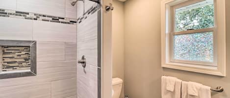 A bathroom with a shower, toilet, and a window with a view of trees.