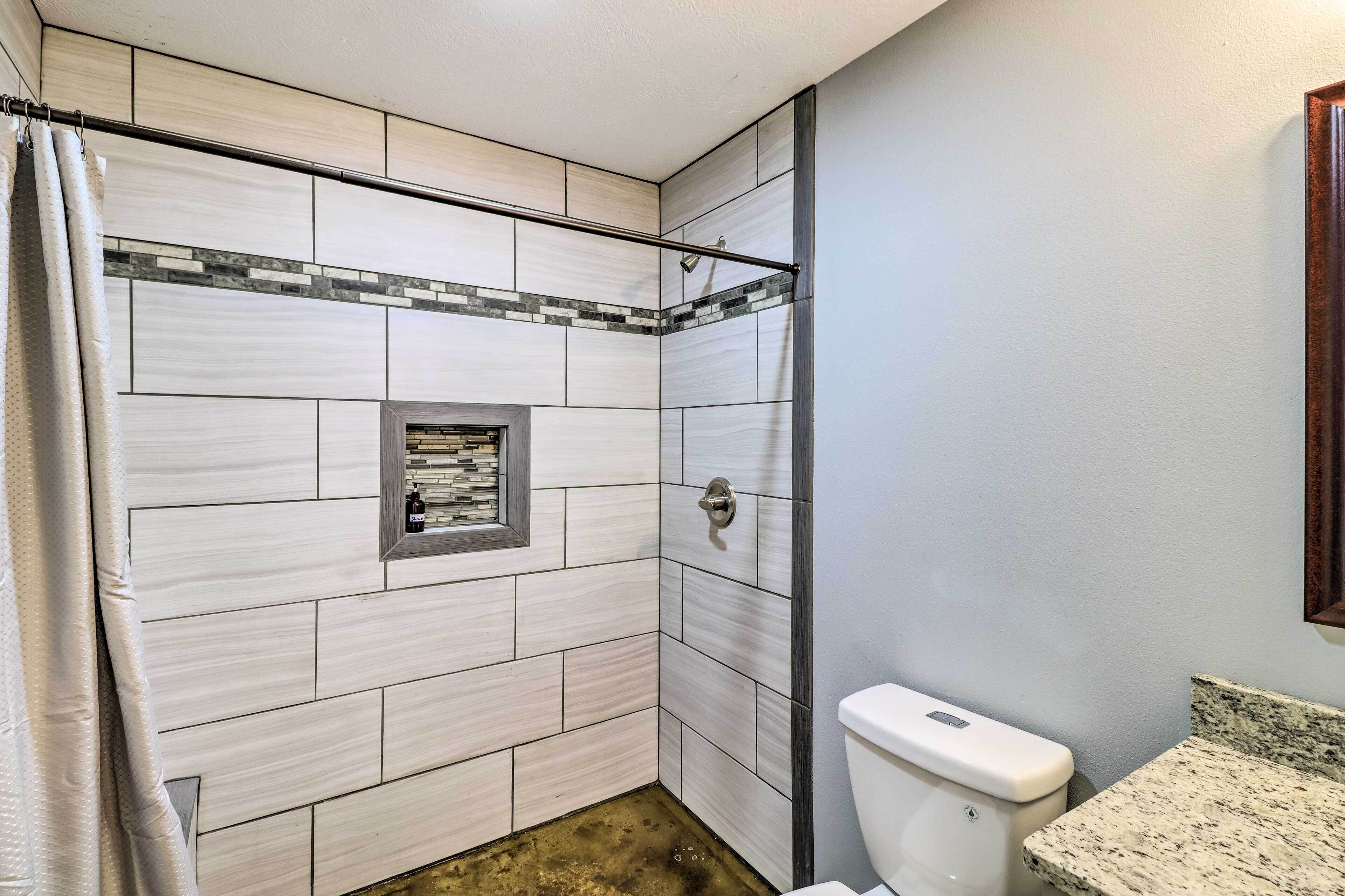 A bathroom with white tiles, a shower area, a toilet, and a granite countertop.