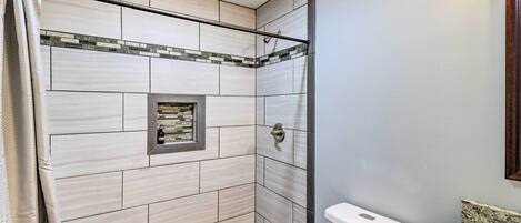 A bathroom with white tiles, a shower area, a toilet, and a granite countertop.