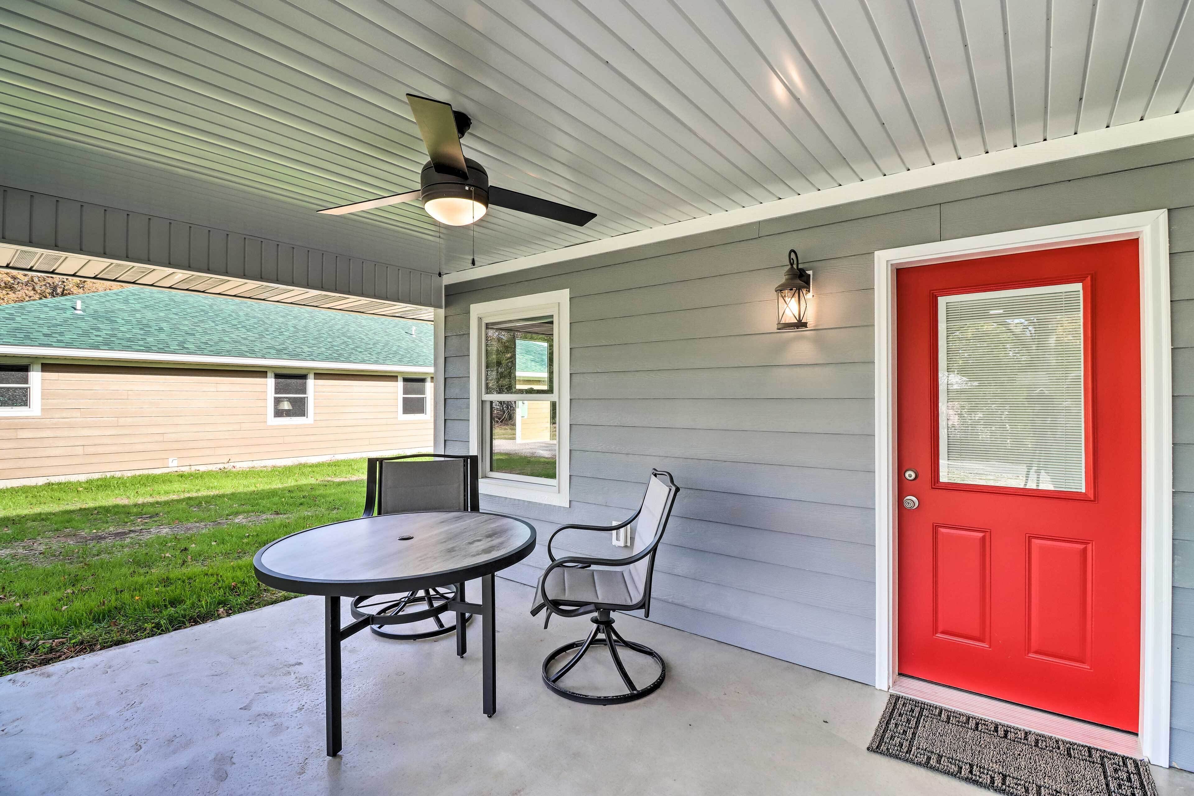 A covered patio with a table and chairs, a red door, and a ceiling fan.