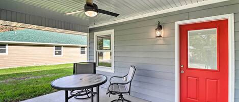 A covered patio with a table and chairs, a red door, and a ceiling fan.