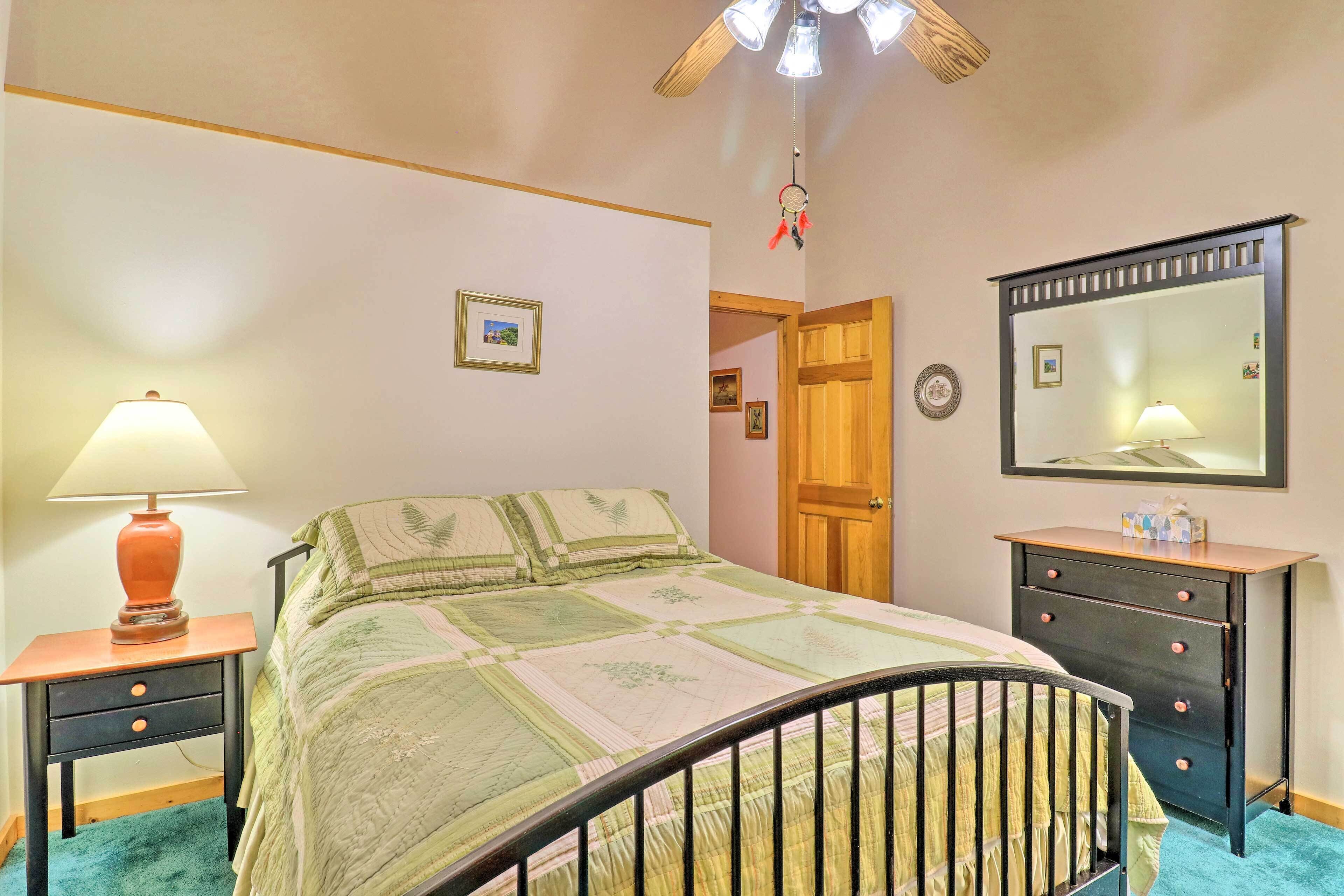 Una camera da letto con un letto, un comodino con una lampada, una cassettiera, uno specchio e una ventola a soffitto.