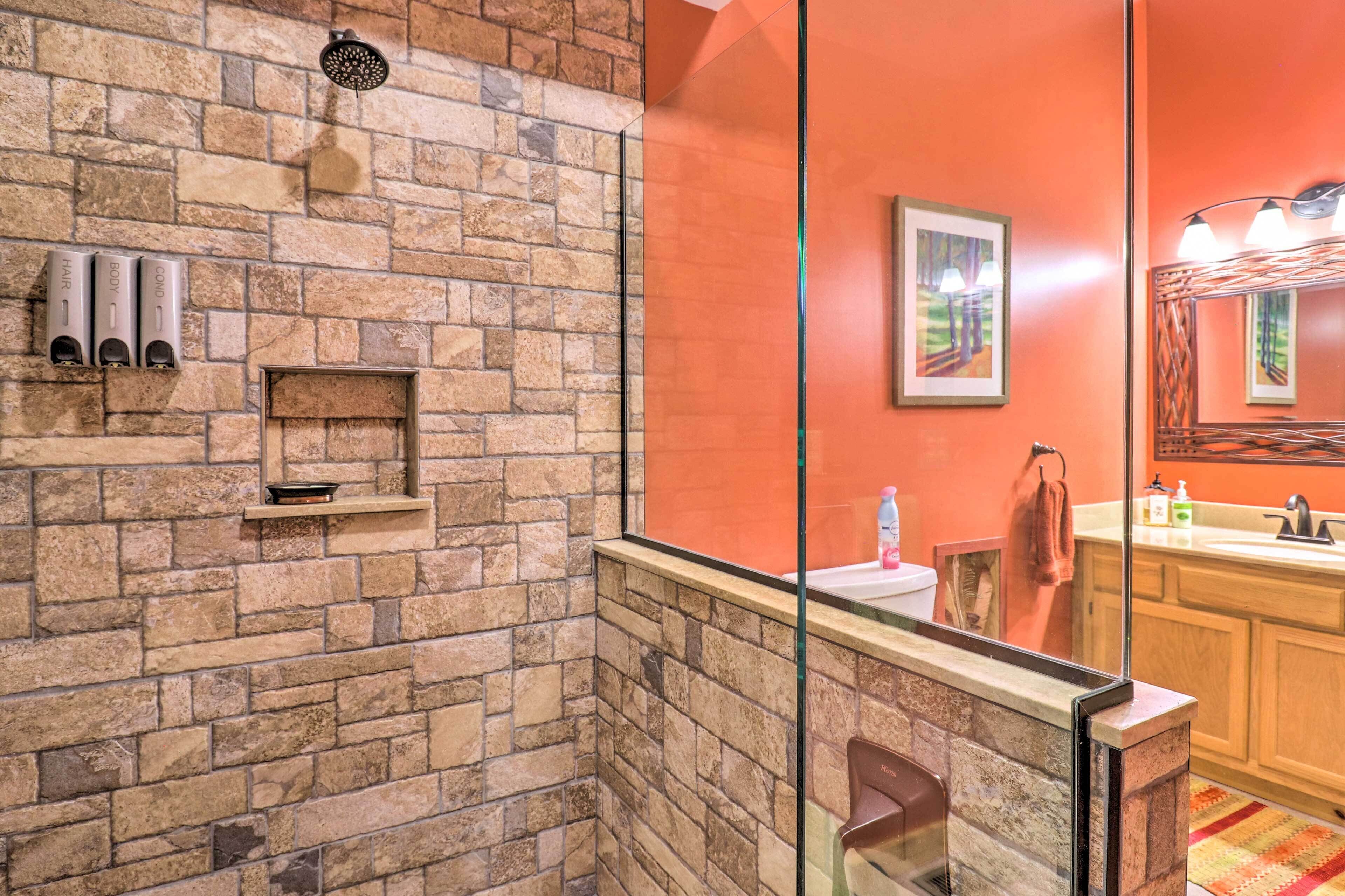 A bathroom with a stone wall, a glass shower enclosure, a wooden vanity with a sink, and a mirror.