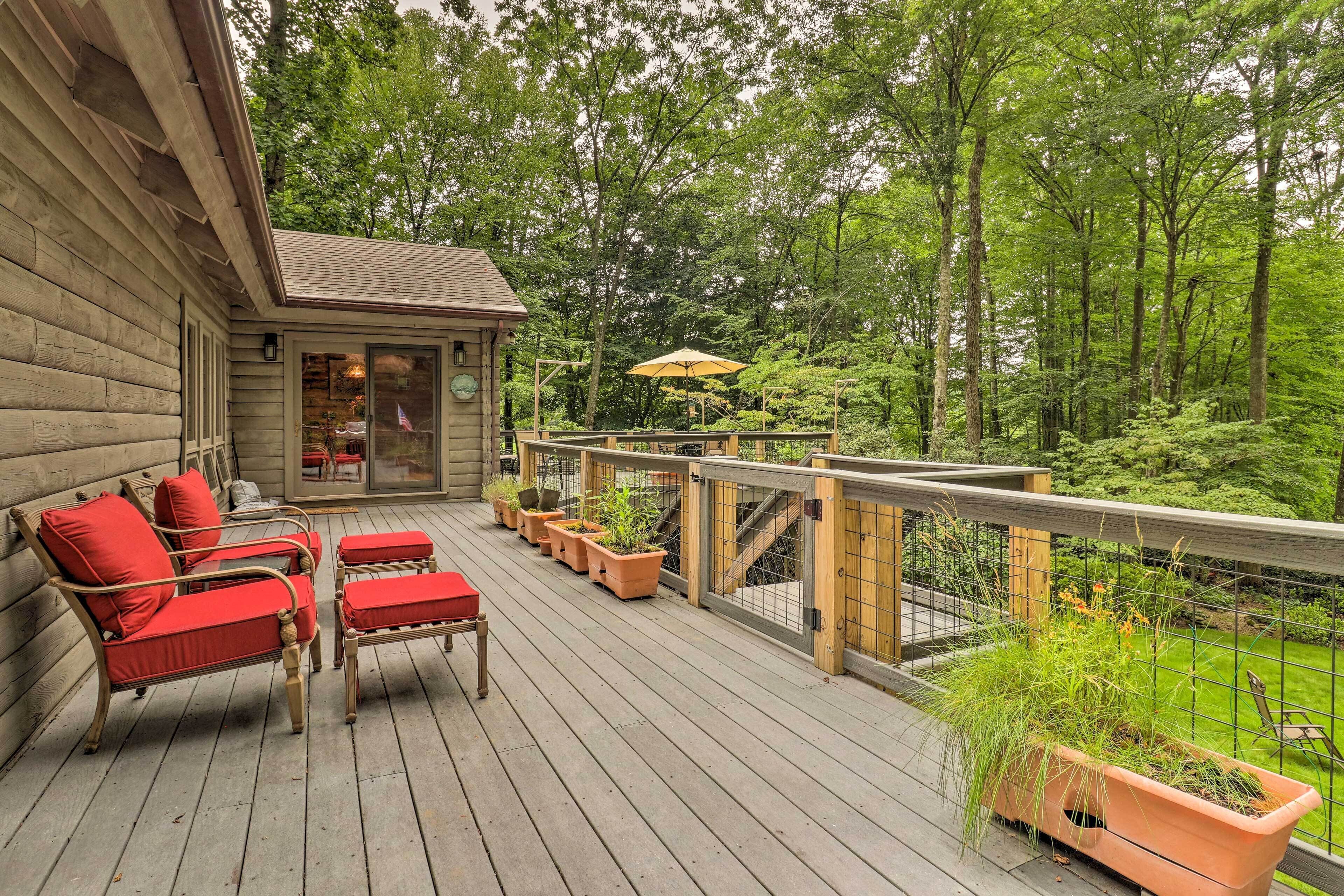 Une terrasse en bois avec des meubles d’extérieur rouges, une porte vitrée donnant sur l’intérieur et une vue sur une zone boisée.