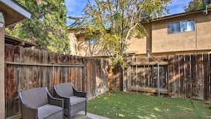 A backyard with a wooden fence, two wicker chairs, and a small lawn area.