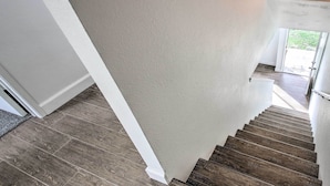 A staircase with wooden steps leading to a landing, white walls, and a view of the outdoors through a glass door.