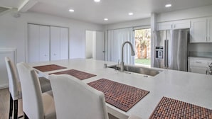 A modern kitchen with white cabinets, a stainless steel refrigerator, and a large island with seating.