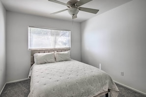 A bedroom with a bed, a ceiling fan, a window with blinds, and a carpeted floor.