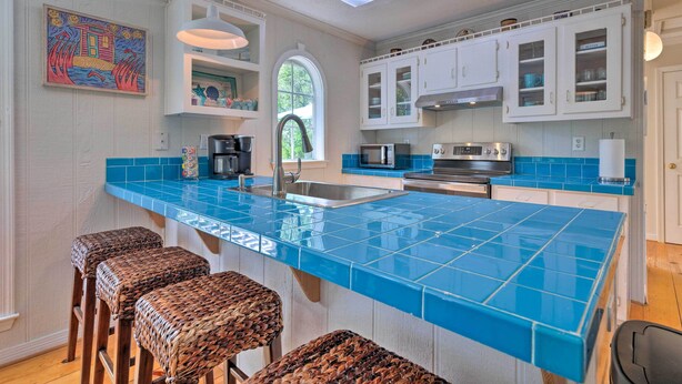 A kitchen with a blue tile countertop, white cabinets, and wicker bar stools. - Charming Dauphin Island Home ~ 1 Mi to Beach! (Dauphin Island)
