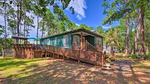 A wooden cabin with a porch and stairs, surrounded by tall pine trees. - Charming Dauphin Island Home ~ 1 Mi to Beach! (Dauphin Island)