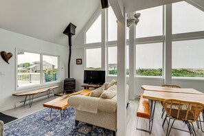 A modern living room with a sofa, wooden tables, and a TV. - Deck + Walk to Beach: Southern Oregon Coast Home! (Gold Beach)