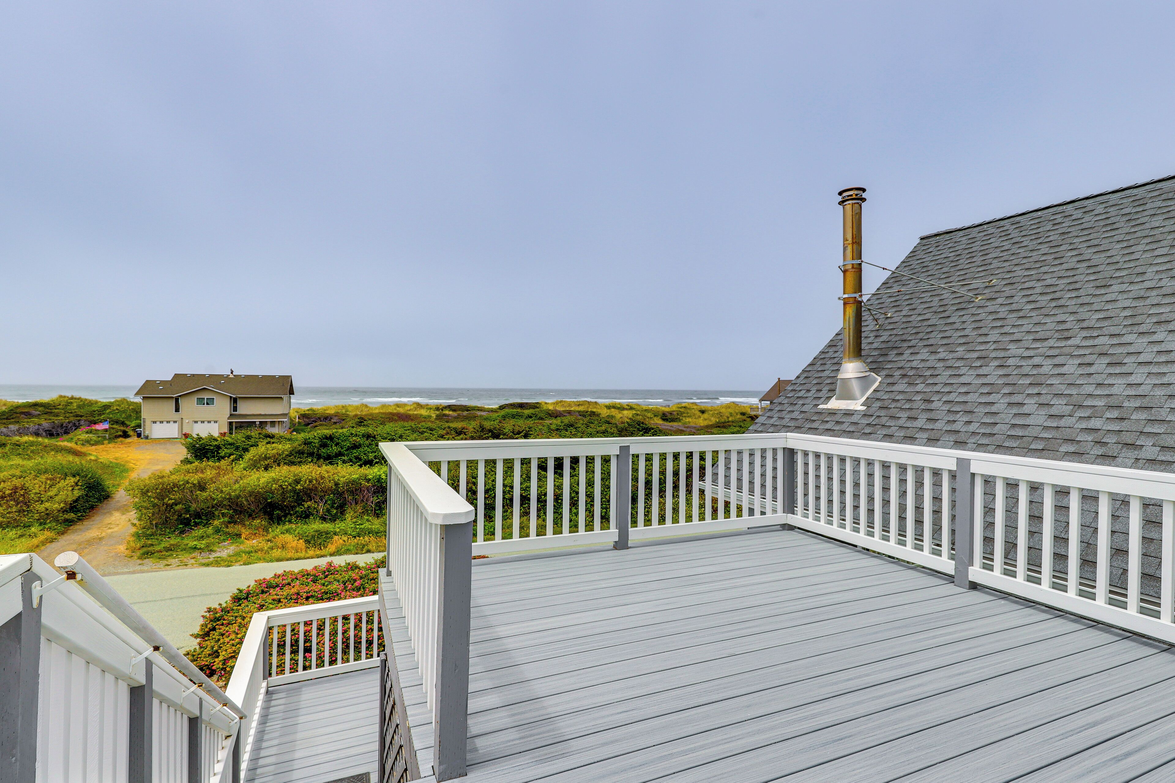 A wooden deck with a white railing overlooking a beach and a house.
