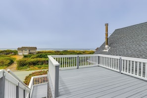 A wooden deck with a white railing overlooking a beach and a house. - Deck + Walk to Beach: Southern Oregon Coast Home! (Gold Beach)