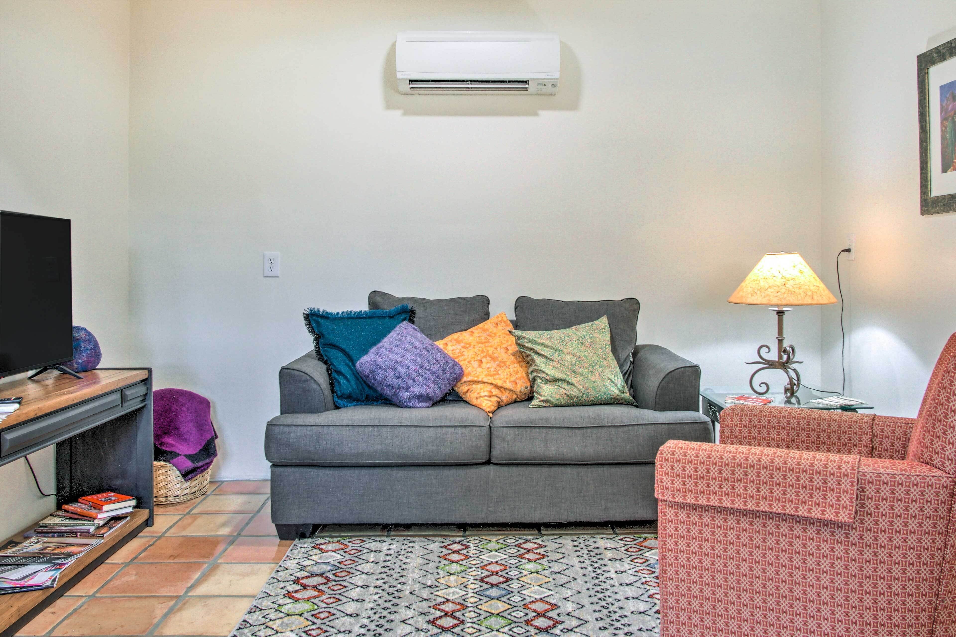 A living room with a grey sofa, a red armchair, a patterned rug, a television, and an air conditioner on the wall.